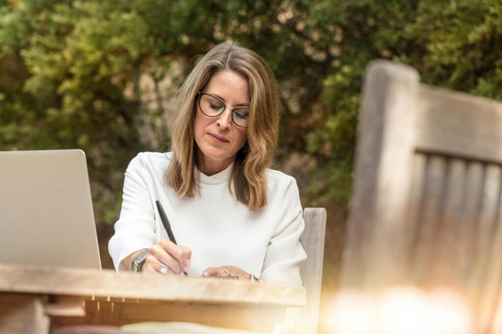 Woman sitting outside at a table, writing in a journal while reflecting on how to stop worrying about past mistakes and move forward.