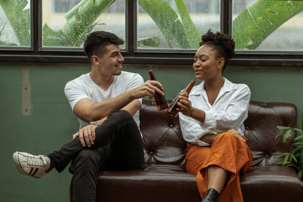 Two friends outdoors clinking bottles in the rain, sharing fun rainy day activities for adults who hate being bored.

