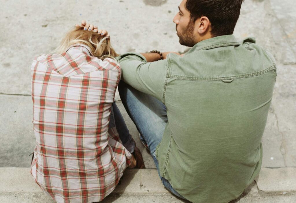 Disappointed woman sitting on the ground outside with her partner, illustrating emotional signs of an unsupportive partner.”