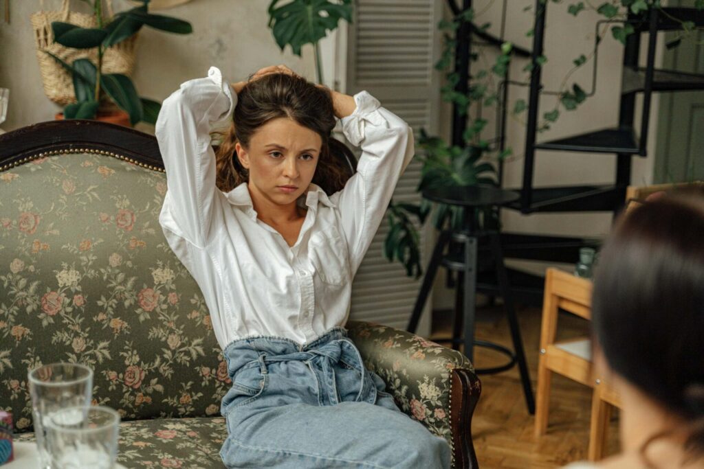 Thoughtful woman sitting on the couch with friends, reflecting on signs of an unsupportive partner in her relationship.