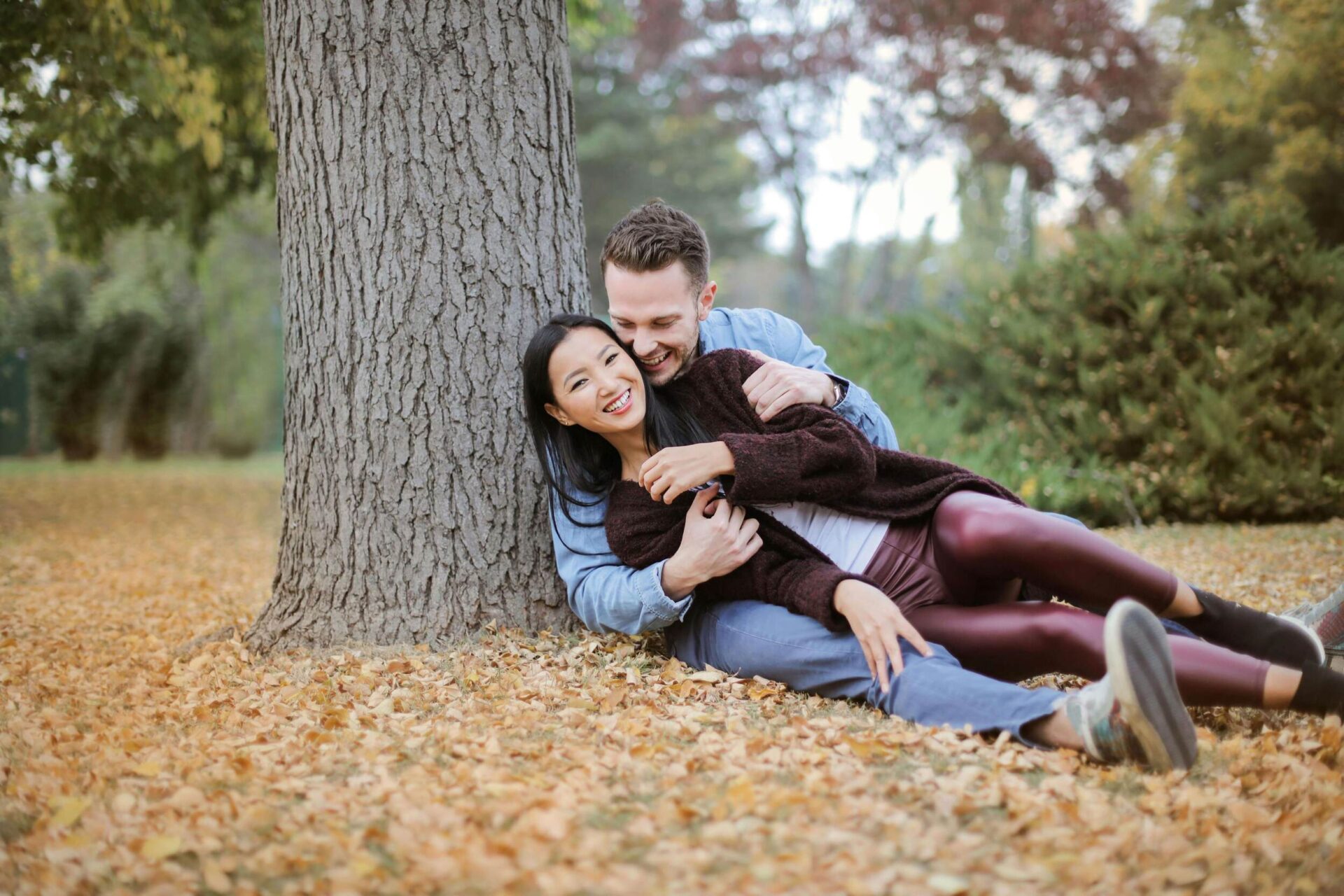 Couple sitting under a tree, smiling and cuddling, symbolizing deep connection and the important things to learn about your partner.
