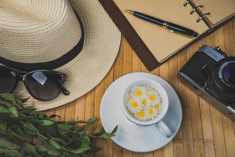 A summer scene with tea, white flowers, a straw hat, journal, pen, sunglasses, and camera—perfect for writing prompts for June and daily reflection.