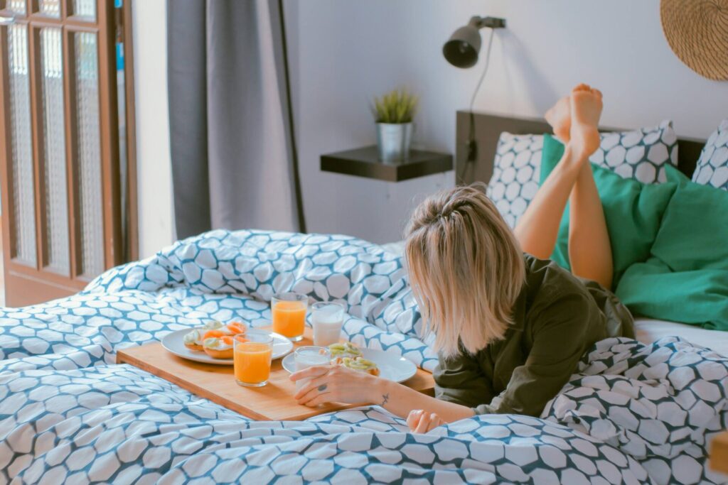 How to feel more grounded in the morning — woman lying on her stomach in bed with a breakfast tray, enjoying a peaceful and mindful start to the day.