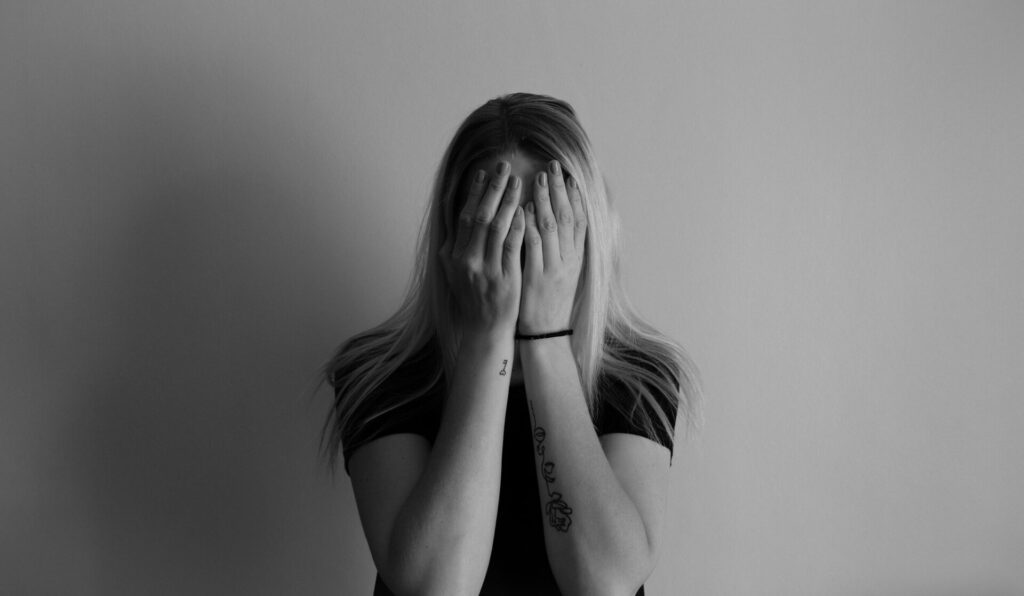 What to do when you feel lost — black and white image of a woman covering her entire face with both hands, overwhelmed and emotionally stuck.