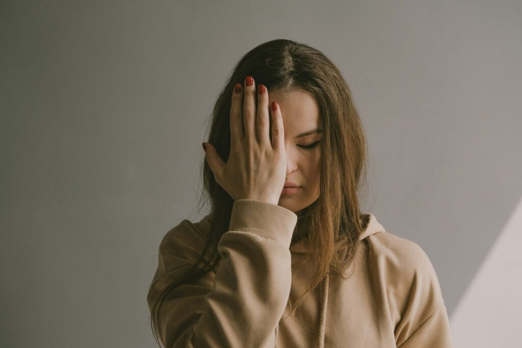 Questions to ask yourself when feeling lost — young woman covering part of her face with her hand, looking down in emotional confusion.
