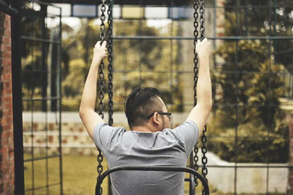 Man sitting alone on a swing in the park, viewed from behind — a calming scene that represents thoughtful self-care ideas for highly sensitive people.