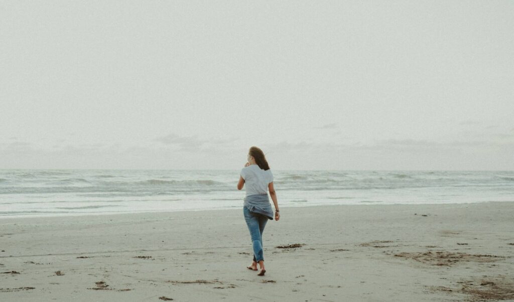 Woman walking alone on an empty beach — peaceful solitude as one of the best self-care ideas for highly sensitive people.

