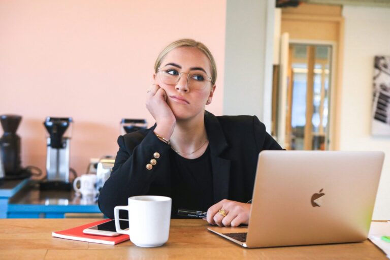 Thoughtful woman dressed formally, sitting in front of a laptop and reflecting, symbolizing the need for journal prompts when you don’t know what you feel.