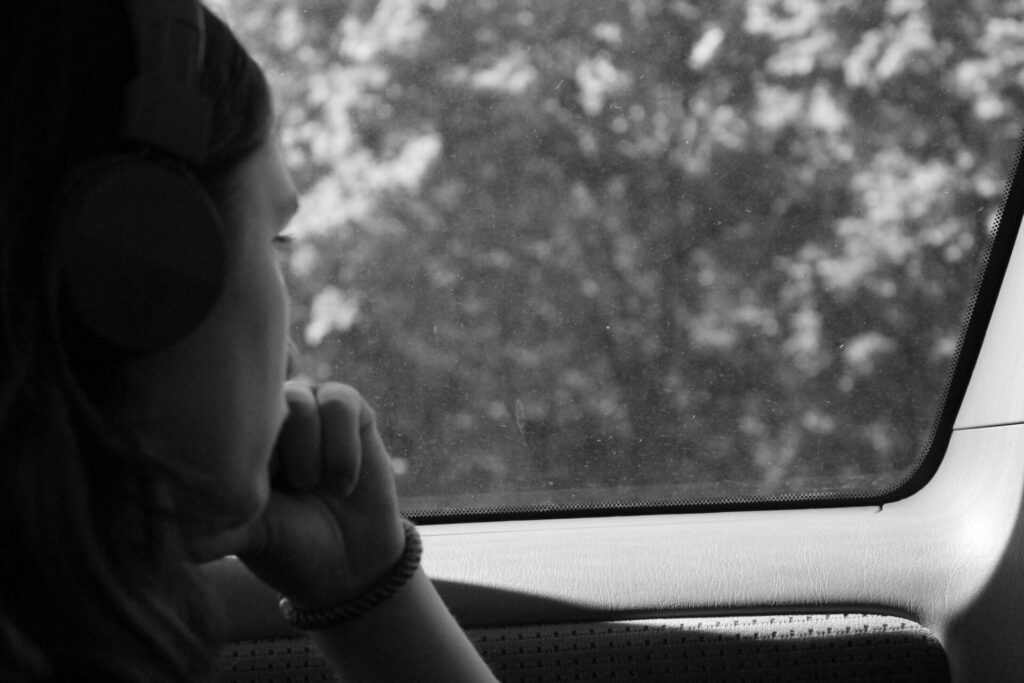 Black and white photo of a woman staring out of a car window, lost in emotions, representing self-reflection with journal prompts when you don’t know what you feel.
