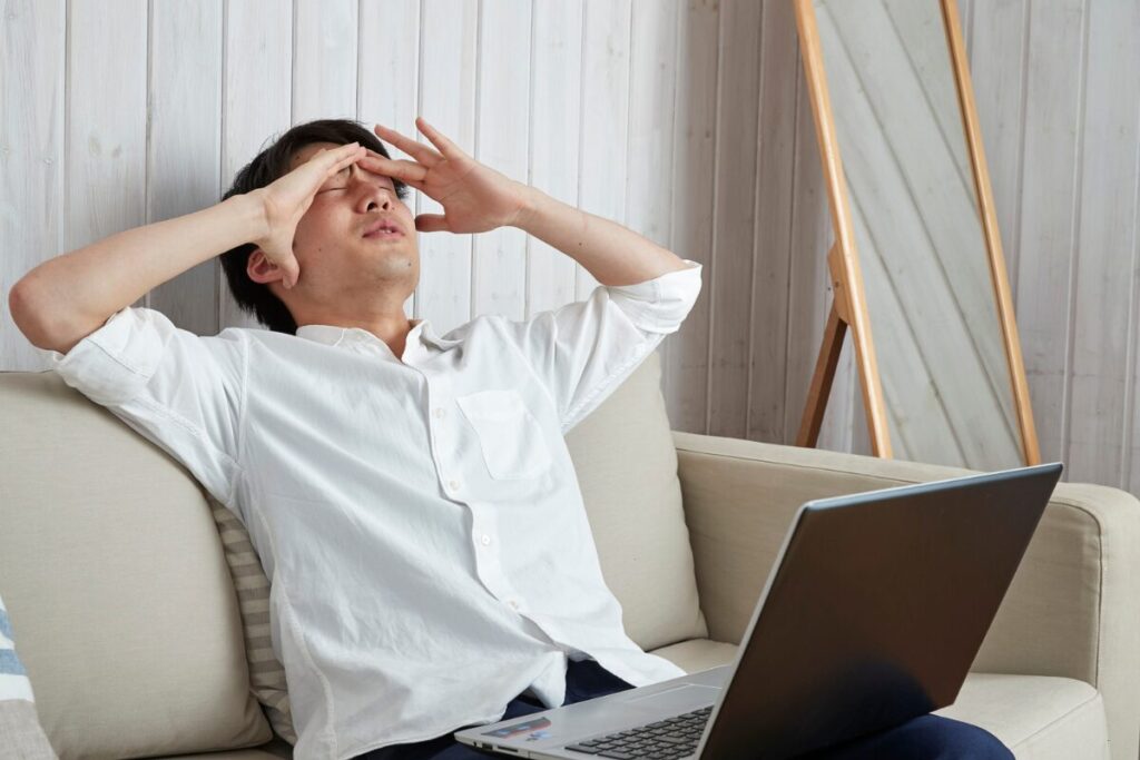 man working on a laptop in the living room, overwhelmed and burned out during the holidays