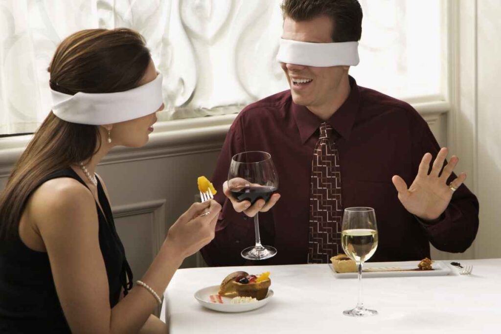 Anniversary date ideas: couple at a restaurant tasting food and drinks blindfolded, having a fun and adventurous date experience