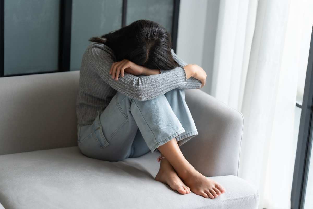 Signs you’re mentally exhausted: a woman sitting on the couch hugging her knees, looking overwhelmed and emotionally drained