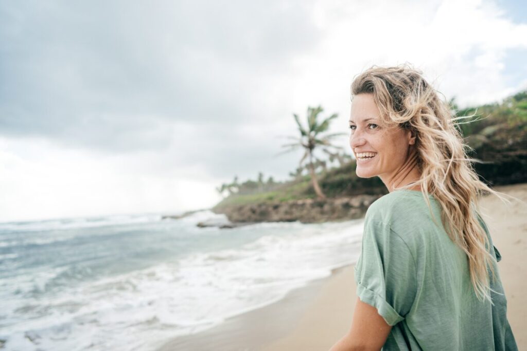 Middle-aged woman smiling alone on the beach, enjoying freedom
